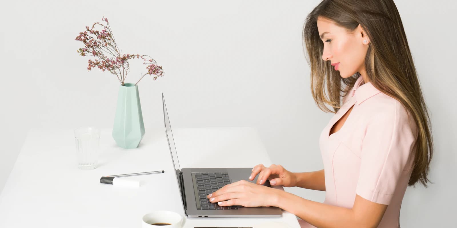 A woman at a clean desk working through a task on her laptop, seen in profile