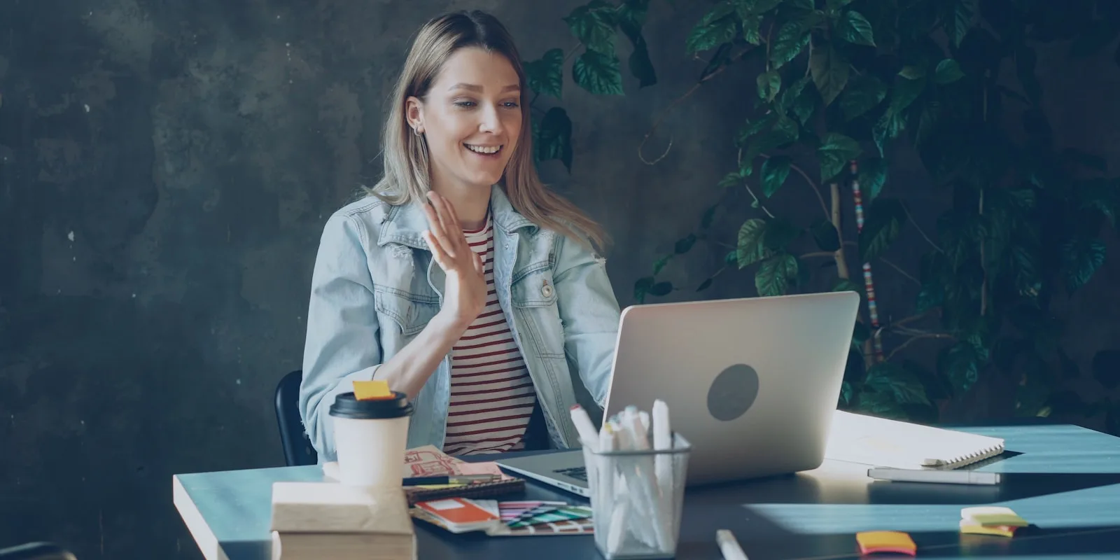 A candidate speaking and gesturing to her laptop during a video interview at her desk
